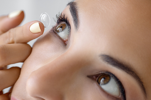 Young woman inserting a contact lens in eye