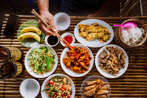 overhead view on male hand picking meat with chop sticks at table with various vietnamese dishes