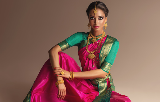 Young gorgeous woman dressed in a traditional Indian costume. Typical national jewlery set consisting of bright necklace and head adornment (tikka) is decorating her neck and head. Indian beauty.