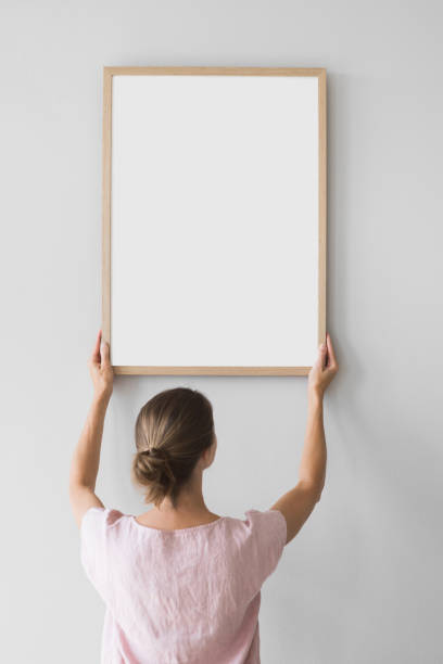 istock Woman carrying blank picture frame against a wall. Artwork mock-up concept 1690594348