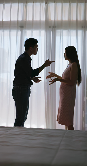 silhouette asian pregnant couple are quarreling near window at home