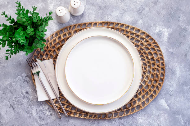 istock Simple dining table setting with white ceramic plate and silver cutlery over rattan round woven placemat on wood background. top view, flat lay 1690602676