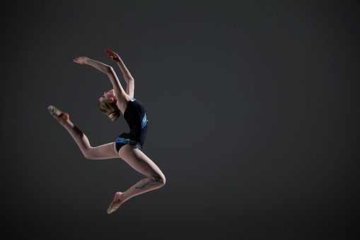 Rhytmic gymnastics female routine on dark background. Figure jump.