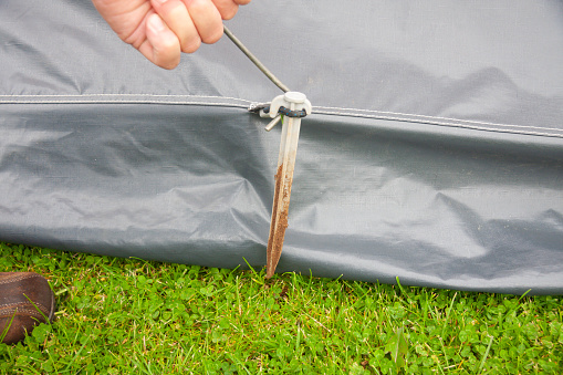 Close up shot of man pulling out tent pegs using a hook tool, the tent pegs have been used to secure the awning in place attached to the caravan to provide more space for the family on vacation