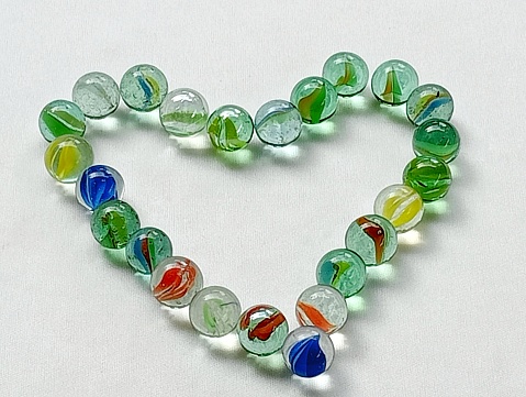 Marbles are children's toys from the 90s. Many marbles placed on the shape of heart on a white background.