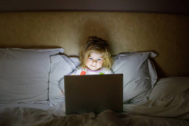 침대에서 노트북에 만화를보고 귀여운 사랑스러운 작은 유아 소녀. 터치 기술이있는 태블릿 장치로 피곤한 아기 아이. 스톡 사진