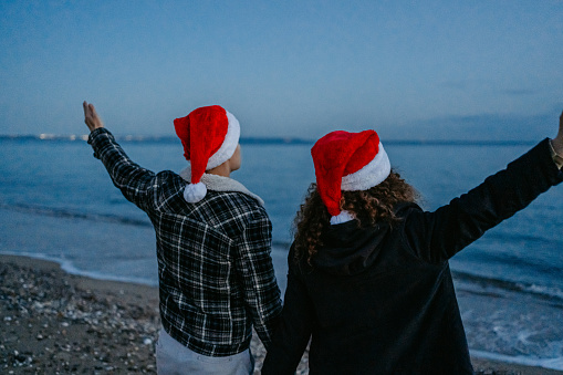 Beautiful young couple enjoying the view of the coastline at dawn in Nea Flogita, Greece. Wearing Santa hats and celebrating Christmas.