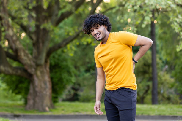istock A young Indian man injured and sprained his back while jogging in a park outside. He stands holding his hand to his body and grimaces in pain 1690681576