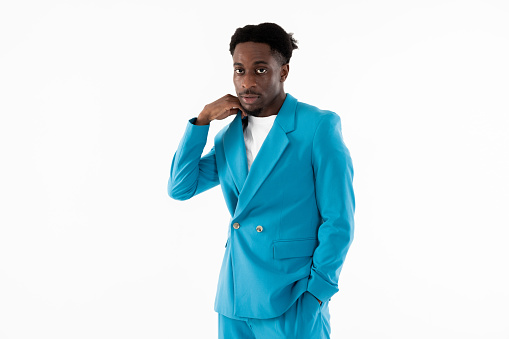Handsome african american buisnessman standing on white background in studio isolated looking at camera wearing smart blue suit and white t-shirt holding hand in pocket.