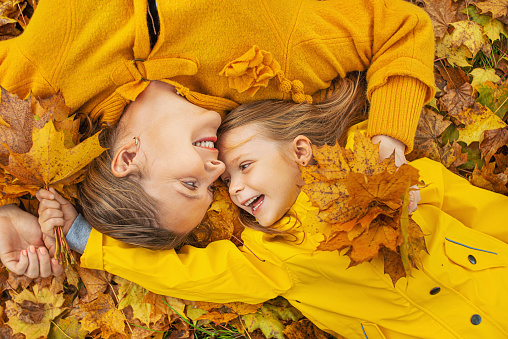 Little girl and her mother playing in the yellow autumn park. Healthy and having fun in golden October concept.