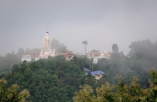 A silhouette of a Standing Buddha statue at Wat Phrathat Doi Kham in Thailand on a foggy day