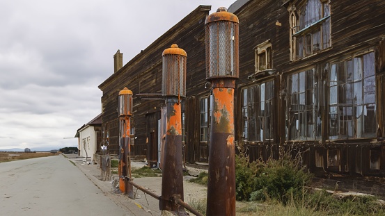 The rust-covered metallic street lamps against a wooden abandoned building on a cloudy day