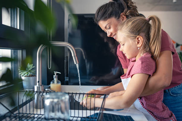 una linda niña ayuda a su madre a lavar los platos - lavar los platos fotografías e imágenes de stock