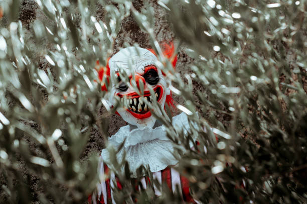 istock mad evil clown hiding behind the branches of a tree 1690717519