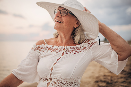 Portrait of a charming senior woman standing on the beach by the sea.