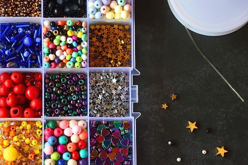 Box with colorful beads, string, wire, chain, scissors, pliers and hammer on dark background. Various jewelry making supplies. Top view.