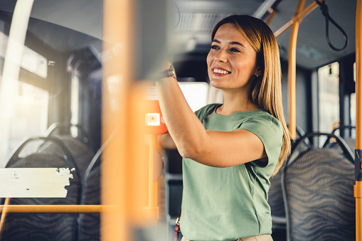 Young woman in a public transport. A young pretty woman standing in a bus. Young adorable joyful woman is standing on the bus.