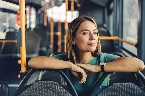 Beautiful woman sitting on the public bus. Woman traveler contemplating outdoor view from window of bus. Young lady on commute travel to work sitting in bus or train.