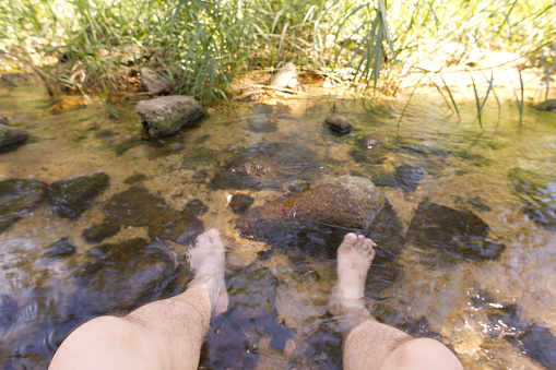 Woman's legs ankle-deep in clear water. Ripple patterns reflect light on water over pebbles
