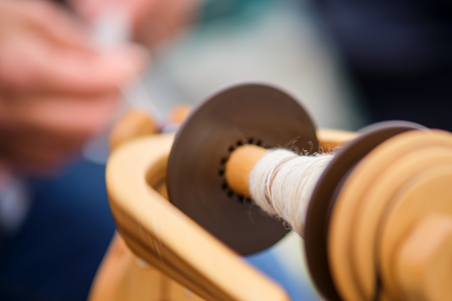 The closeup shot shows a hand spinning thread on a vintage spinning wheel.