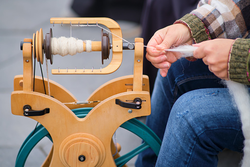 horizontal view of an outdoors shop of wools dyed with natural dyes and an antique pedal wooden spinning wheel in the foreground