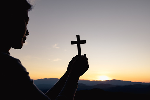 Silhouette of christian woman hand praying, woman holding a crucifix praying, spirituality and religion, woman praying to god. Christianity concept.