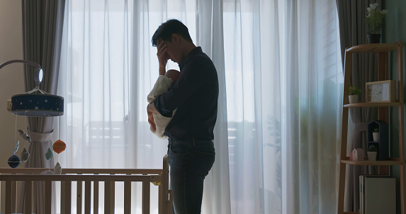 silhouette asian man holding his baby feel depressed about being new dad while standing by windows