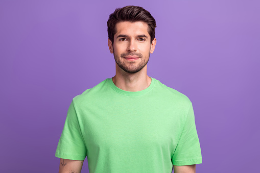 Photo of friendly confident handsome man with stubble dressed green t-shirt standing look at camera isolated on purple color background.