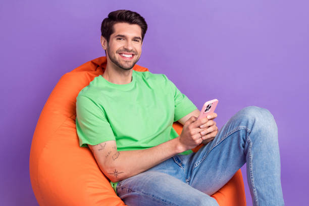 istock Photo of chilling comfortable bean bag event zone sitting young handsome model guy order pizza phone online isolated on purple background 1690852042