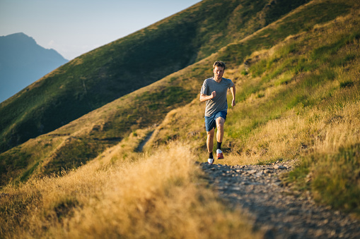 Trail runner bounds along a mountain pathway at sunrise, Ticino Canton