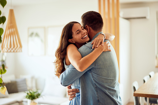 A brunette woman hugging her man, looking happy, being at home.
