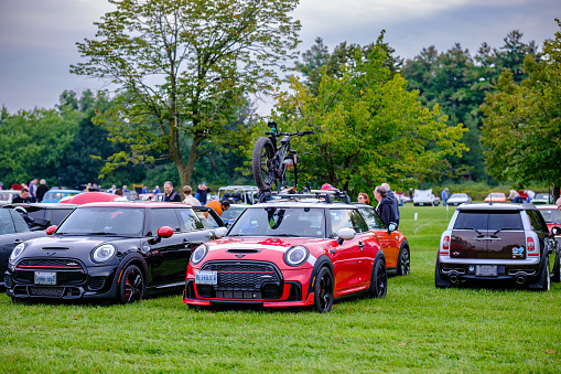 Oakville, Ontario, Canada- September 17, 2023.  Chili red colour MINI COOPER with fat bike on the roof  on the lawn in public park. This is the third generation model F56 JCW, since BMW took over iconic brand of MINI. MINI featured in the photo is John Cooper Works model, the most powerful 2 door version. MINI COOPER cars and fans on British Car Day show  in public park in suburb of Toronto, Canada. British Car Day is the largest British car show in North America. Over 1000 cars on display and 50 vendors. Held the 3rd Sunday of September at Bronte Park, Oakville, Ontario. Mini car has been around since 1959 and has been owned and issued by various car manufacturers.