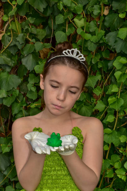 a sweet GIRL PLAYING  in a garden to be  a PRINCESS AND her pince is a PLASTIC Frog