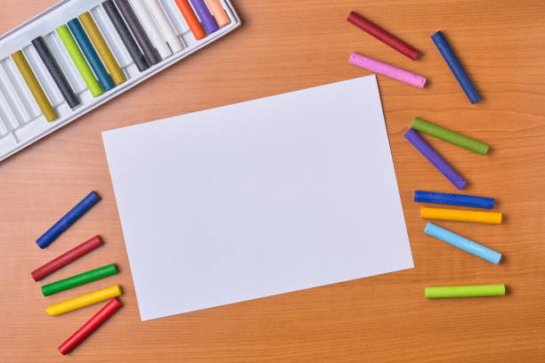 oil pastel crayons and an empty or blank white paper on desk, crayons scattered and set box in the background, taken straight from above with copy space
