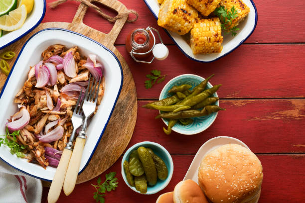 istock Pulled bbq chicken with baked onions on serving platter, bbq corn, pickles, chili peppers and buns for hot dogs and burgers, tomato sauce. Traditional American grilled summer bbq sandwiches dishes. 1690917538