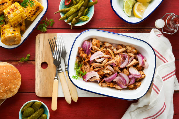 istock Pulled bbq chicken with baked onions on serving platter, bbq corn, pickles, chili peppers and buns for hot dogs and burgers, tomato sauce. Traditional American grilled summer bbq sandwiches dishes. 1690919225