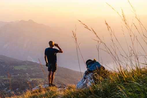 Hiker drinking from water bottle on mountain peak during sunrise