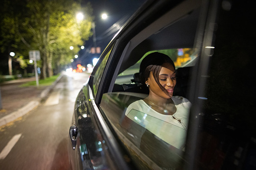 Beautiful black woman riding in a car back seat in city at night.