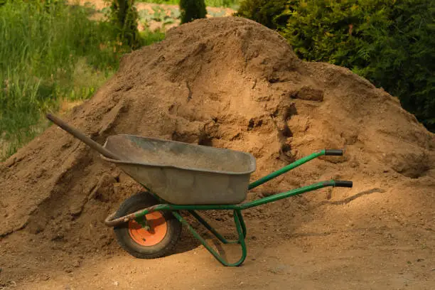 Photo of Garden-wheelbarrow with near a pile of sand on a farm.