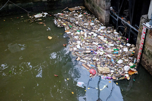 Bangkok, Thailand, December 28, 2018. A polluted body of water filled with trash, including plastic bottles and cans, against a concrete wall.