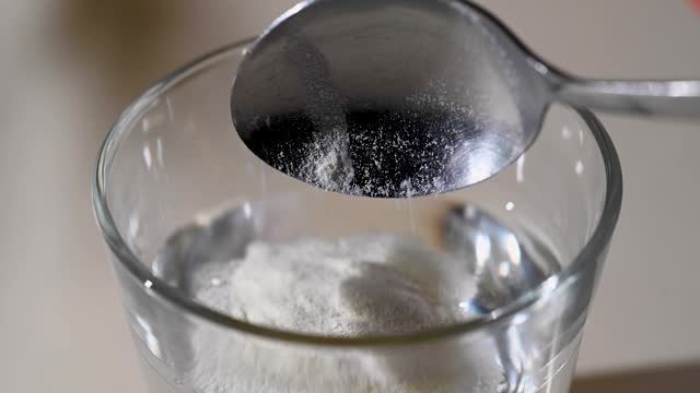 Adding collagen powder in a glass of water. Food supplements for wellbeing
