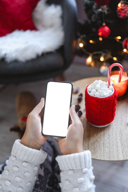 istock Close up smartphone with empty screen mockup on holiday background with Christmas tree, customer holding phone in hand, shopping online, purchasing gifts, searching information, browsing apps 1690935266