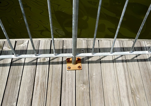 A iron metal fence with a striped wooden floor beside a pond in the park