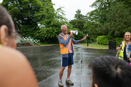 Man wearing a reflective jacket with a megaphone organising a group of running participants taking part in a fun run in Leazes Park in Newcastle upon Tyne in the North East of England.