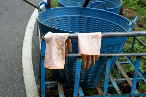 Close up a orange rubber gloves in blue plastic basket on the trolley the street in the park