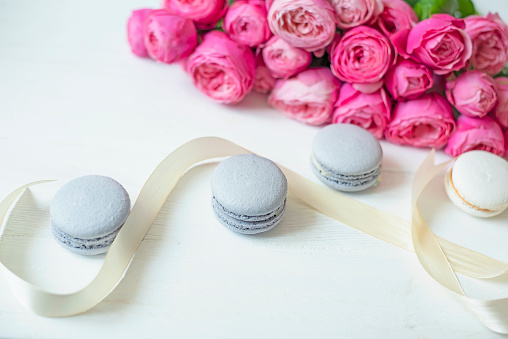 pink peony roses and sweet macarons on a white wooden background