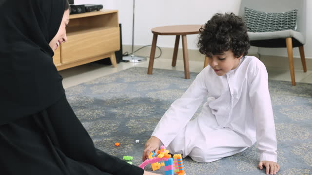 Little boy in thawb playing toys with mom in hijab