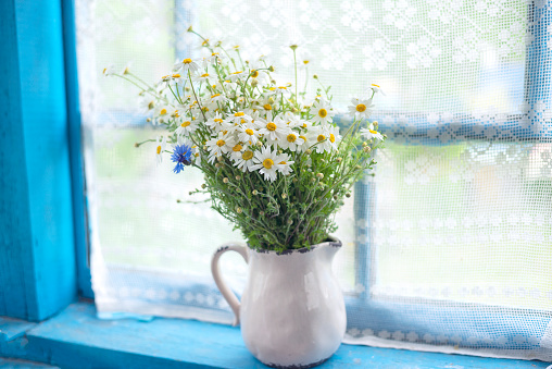 A simple field bouquet of daisies on an old village window. Soft focus, summer mood and soft sunlight.