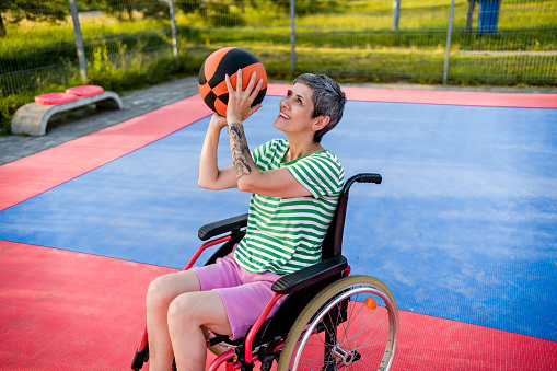 Disabled mature woman in a wheelchair playing basket on a basketball court