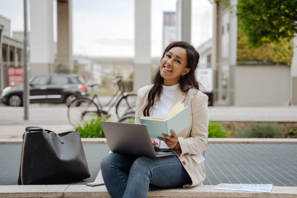 istock Smiling businesswoman using laptop computer holding notepad looking at camera working outdoors 1690938544